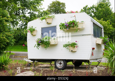 Vecchia roulotte con molti fiori appesi in vasi Foto Stock