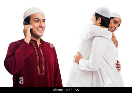 Uomo che parla di un cellulare con i suoi amici che abbraccia ogni altro durante il festival di Eid Foto Stock