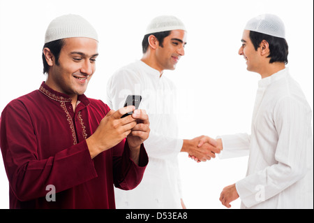 Uomo di messaggistica di testo su un telefono cellulare con i suoi amici si stringono la mano in background durante il festival di Eid Foto Stock