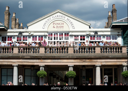 La folla guarda buskers presso il Punch e Judy Pub, nella parte anteriore del St Pauls Chiesa, Covent Garden Plaza, London Foto Stock