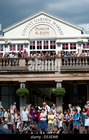 La folla guarda buskers presso il Punch e Judy Pub, nella parte anteriore del St Pauls Chiesa, Covent Garden Plaza, London Foto Stock