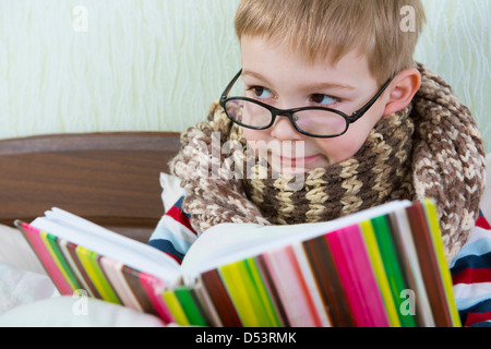 Piccolo ragazzo malato in bicchieri libro di lettura a letto Foto Stock