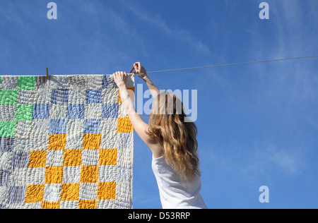 Longhaired giovane donna mettendo un luminoso counterpane su un abbigliamento in linea per asciugare in una brezza. Foto Stock