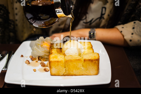 Sciroppo essendo versato su una pallina di gelato alla vaniglia sul pane tostato Foto Stock