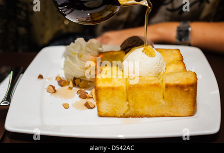 Sciroppo essendo versato su una pallina di gelato alla vaniglia sul pane tostato Foto Stock