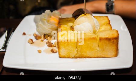 Sciroppo essendo versato su una pallina di gelato alla vaniglia sul pane tostato Foto Stock