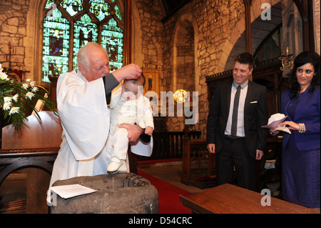 Bambino giovane che viene battezzato da un vicario e guardato dai genitori Inghilterra UK. Inghilterra Inghilterra battesimo bambini chiesa servizio di famiglia battesimo Foto Stock