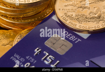 Oro massiccio monete in contrasto con la parola di addebito sulla plastica carta di credito suggerendo problemi di debito Foto Stock