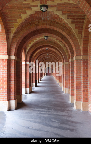 Rosso mattone di gomma rivestita passerella coperta in mattoni ad arco che conduce a una porta in corrispondenza della estremità lontana qualche pioggia bruciato nel lato modulo Foto Stock