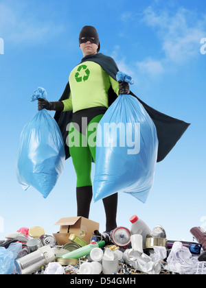 Il supereroe Eco tenendo due sacchetti di plastica piena di rifiuti domestici in piedi sul cumulo di rifiuti - rifiuti Nozione di segregazione Foto Stock