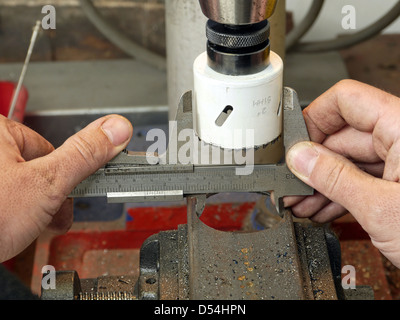 Vista dettagliata del macchinista lavoratore mani prendendo una misurazione del diametro del foro ricavato in un pezzo di metallo utilizzando pinza Foto Stock