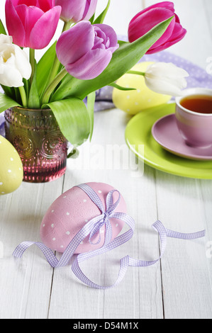 Rosa, viola e bianco tulipani in un vaso di vetro con le uova di pasqua su sfondo di legno Foto Stock