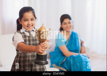 Ritratto di una ragazza che mostra il suo trofeo con sua madre in background Foto Stock