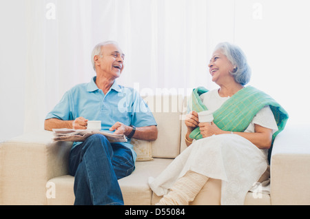 Coppia senior bere il tè con un giornale e sorridente a casa Foto Stock