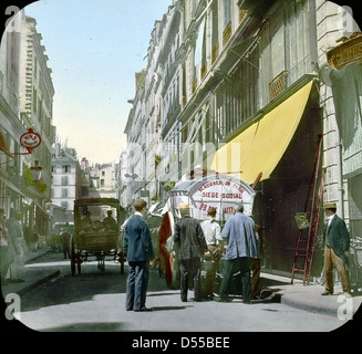 Una fotografia del 1900 di una scena di strada durante l'esposizione di Parigi, identificata come Rue Gomboust vicino Saint Honor. L'immagine cattura la vibrante atmosfera di Parigi alla fine del secolo, con persone e attività di mercato tipiche del periodo. Foto Stock