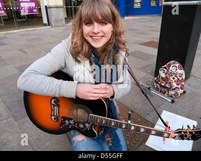 Giovane femmina attraente busker Sophie giocando la sua chitarra su un Cardiff city centre street Wales UK Foto Stock