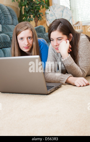 Due ragazze adolescenti la posa sul pavimento con un computer portatile. Tappeto a fondo fornisce un sacco di spazio di copia Foto Stock