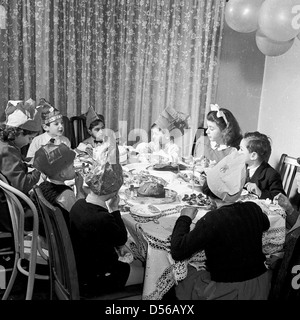 Storico degli anni cinquanta. In Inghilterra. Bambini's tea party. Piccolo gruppo di bambini sedersi intorno ad un tavolo gustando una cena di compleanno e party. Foto Stock