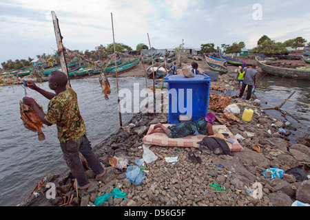 Uomo di essiccazione di persico del Nilo per l' esportazione e la donna posa sul materasso in attesa per le barche per tornare, Remba Island, il lago Victoria, in Kenya. Foto Stock