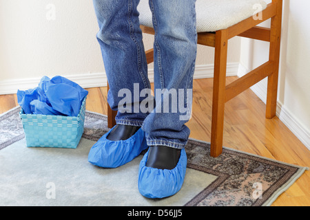 Gambe maschio indossano jeans visto dalle ginocchia a terra blu da indossare protezioni chiamato babbucce su entrambi i piedi. Pavimenti blu babbucce sulle scarpe Foto Stock