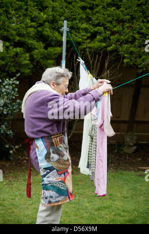 Donna anziana di stendere panni lavati per essiccamento naturale nel giardino in una giornata di vento Foto Stock