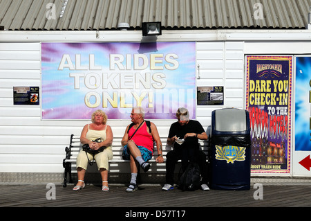 Tre persone sedute sul molo di Brighton godendo di una calda giornata di sole Foto Stock