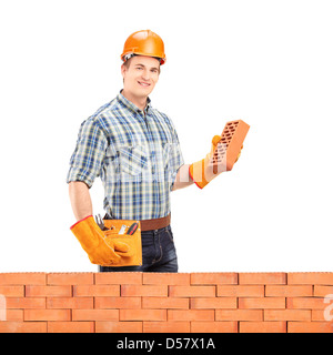 Maschio lavoratore manuale con casco tenendo un mattone dietro un muro di mattoni isolati su sfondo bianco Foto Stock