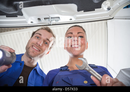 Due meccanici di dare una occhiata sotto il cofano di un'auto in un garage per la riparazione Foto Stock