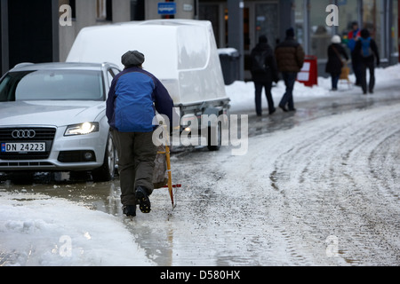 Donna spingendo la slitta di kick out shopping su ghiaccio coperto storgata strada principale dello shopping di Honningsvag finnmark Norvegia europa Foto Stock