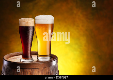 Due bicchieri di birra su di un barile di legno. Di colore giallo scuro dello sfondo con un gradiente. Foto Stock