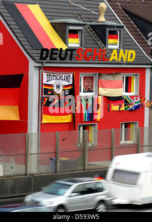 Für die Fußball Weltmeisterschaft in Südafrika hat am Donnerstag (10.06.2010) ein Essener Hauseigentümer direkt an der Autobahn 40 sein Haus geschmückt. Mit Deutschlandfahnen und Weltpokal dem auf dem Dach es ist ein Blickfang für viele tausend Pendler, die jeden Tag auf dem Weg zur Arbeit un diesem Haus vorbei kommen.. Foto: Roland Weihrauch dpa/lnw Foto Stock