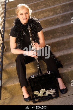 Una femmina Street Performer si siede sui gradini vicino al clarinetto caso con suggerimenti Foto Stock