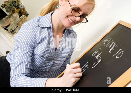 Bellissima femmina docente scrive un messaggio sulla lavagna dicendo Benvenuti alla biologia Foto Stock