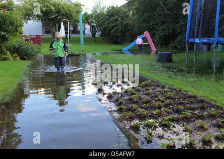 Handewitt, Germania, un ragazzo corre in stivali di gomma attraverso un giardino inondato Foto Stock