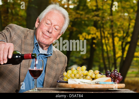 Senior uomo godendo di vino rosso all'aperto in autunno foresta. Foto Stock
