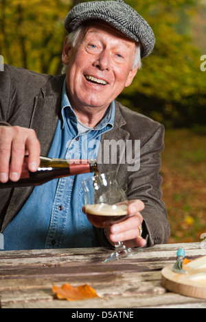 Senior uomo godendo di birra scura e formaggio all'aperto in autunno foresta. Foto Stock