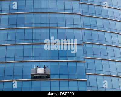 Detergenti per finestre lavorando su una lastra di vetro rivestita in edificio per uffici a Bruxelles, in Belgio Foto Stock