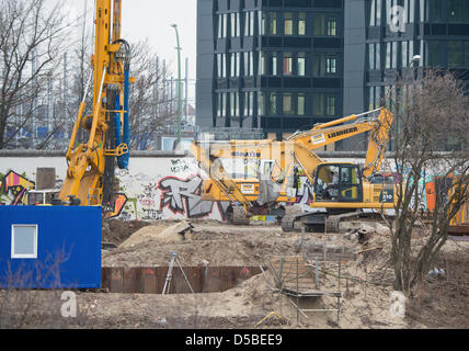 Costruzione macchine lavorano dietro il muro di Berlino a East Side Gallery di Berlino, Germania, 28 marzo 2013. Quattro elementi di parete sono stati rimossi per rendere possibile un accesso a un sito in costruzione. Un investitore piani per la costruzione di un alto edificio di appartamenti sul grafico a destra accanto al fiume Sprea. Foto: SOEREN STACHE Foto Stock