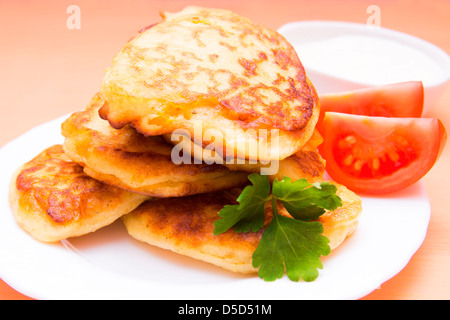 Patate fritte frittelle sulla piastra bianca con verdure e guarnite di panna acida Foto Stock