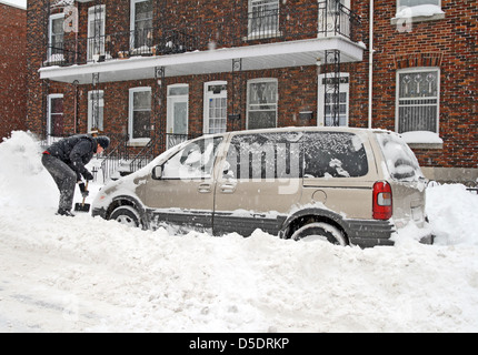 L'uomo spalare e rimozione di neve dalla sua vettura durante una forte tempesta di neve. Foto Stock