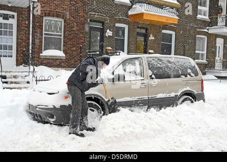 L'uomo spalare e rimozione di neve dalla sua vettura durante una tempesta di neve. Foto Stock
