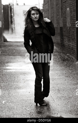 Donna in oscuramente vestito camminando giù la pioggia inzuppato alley Foto Stock