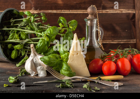 Aglio, il formaggio e i rossi pomodori ciliegini sul tavolo di legno con basilico fresco e olio d'oliva annata in bottiglia di vetro Foto Stock