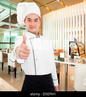 Il giovane chef con il pollice fino gesto nel ristorante Foto Stock