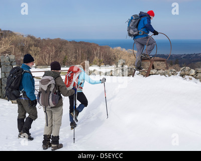 Walkers escursionismo su neve profonda deriva dal montante della scala su una parete sul bordo settentrionale del Parco Nazionale di Snowdonia, Galles del Nord, Regno Unito Foto Stock