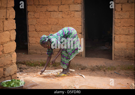 Donna africana in abito di stampa prepara il cibo per il pranzo da lei in mattoni di fango casa in Camerun Foto Stock