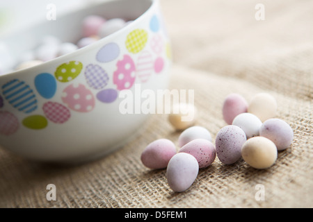 Una ciotola di pasqua mini uova accanto a una manciata di uova di cioccolato, collocato su un marrone sfondo testurizzata Foto Stock