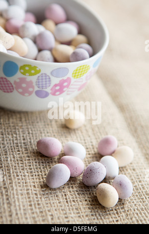 Una ciotola di pasqua mini uova accanto a una manciata di uova di cioccolato, collocato su un marrone sfondo testurizzata Foto Stock