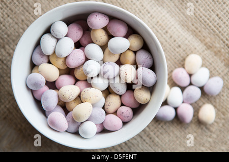 Una ciotola di pasqua mini uova accanto a una manciata di uova di cioccolato, collocato su un marrone sfondo testurizzata Foto Stock