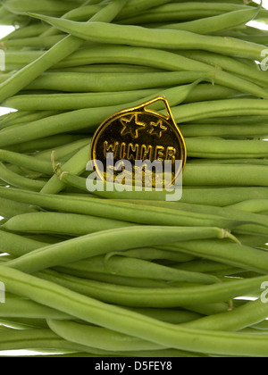 Fagioli verdi con una medaglia d'oro, pendente su uno sfondo di legno Foto Stock